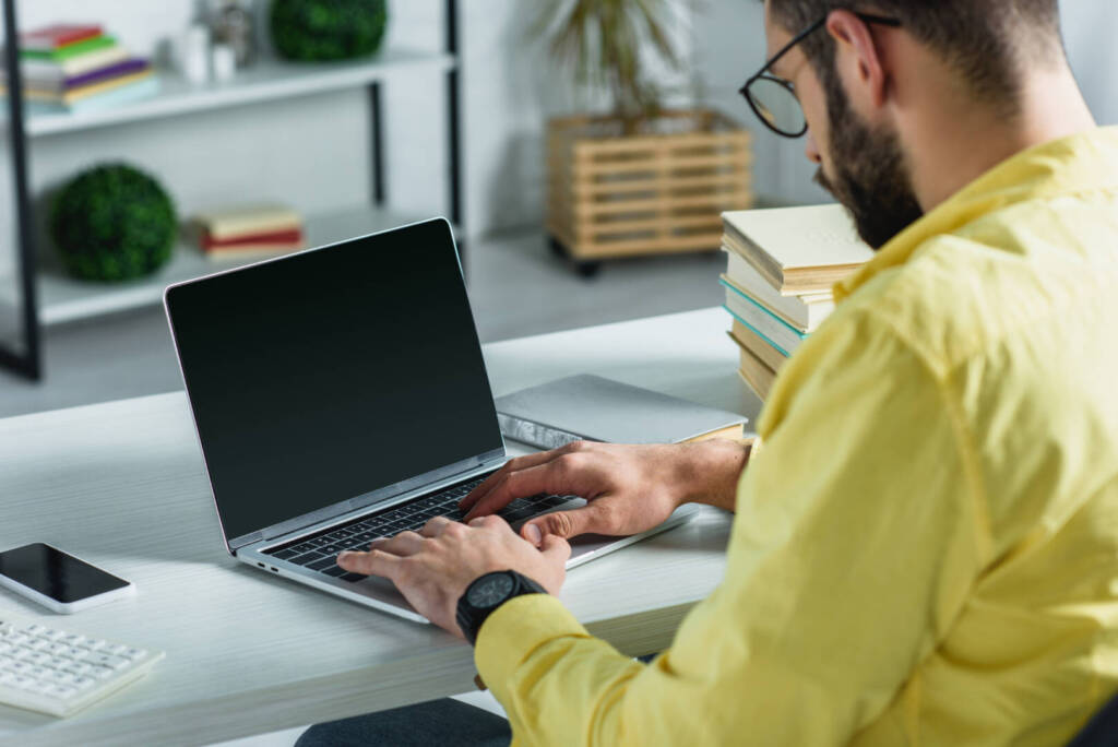 uomo barbuto che guarda il computer portatile con schermo vuoto in un ufficio moderno